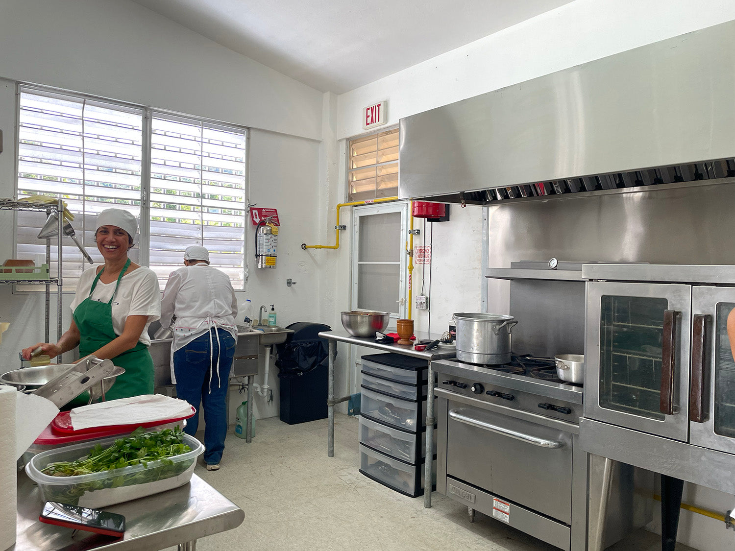 dos cocineras en la Cocina del depa, con comida preparada en cajas y cocinando en la estufa