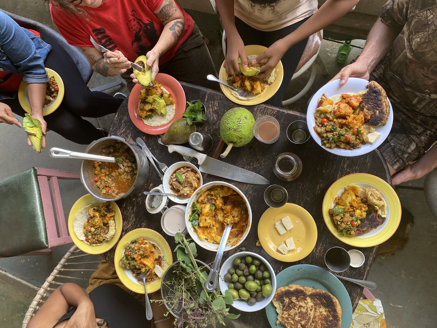 Imagen desde arriba mostrando platos variados con comida y manos cortando aguacates.