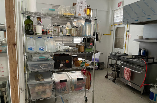 estantes llenas de comida y equipo para cocinar, con la estufa y fregadero en el fondo
